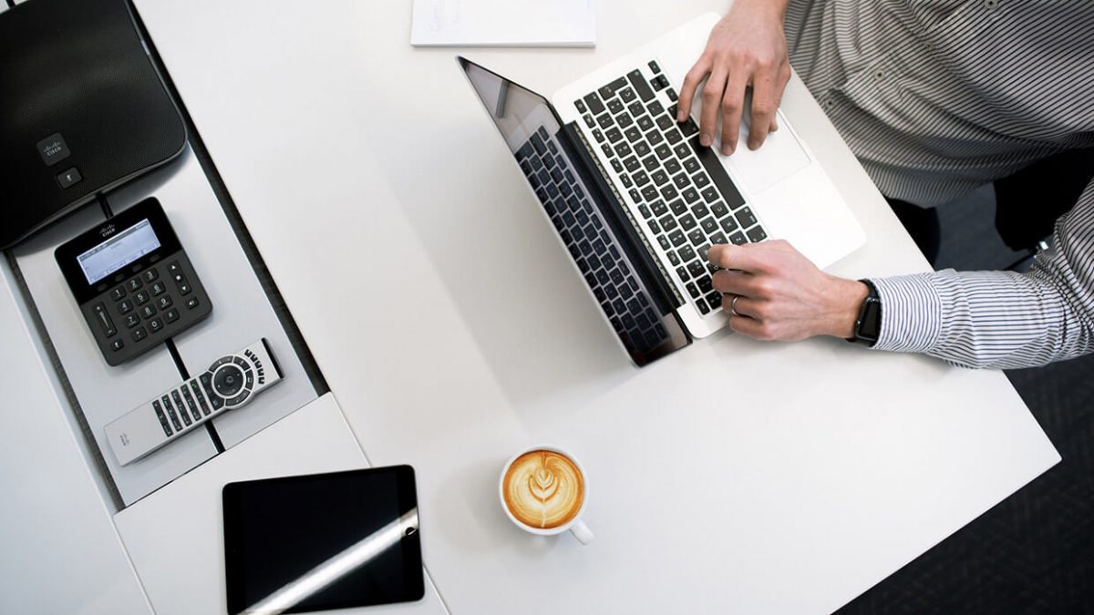 Person working on a laptop with coffee nearby on a clean desk.