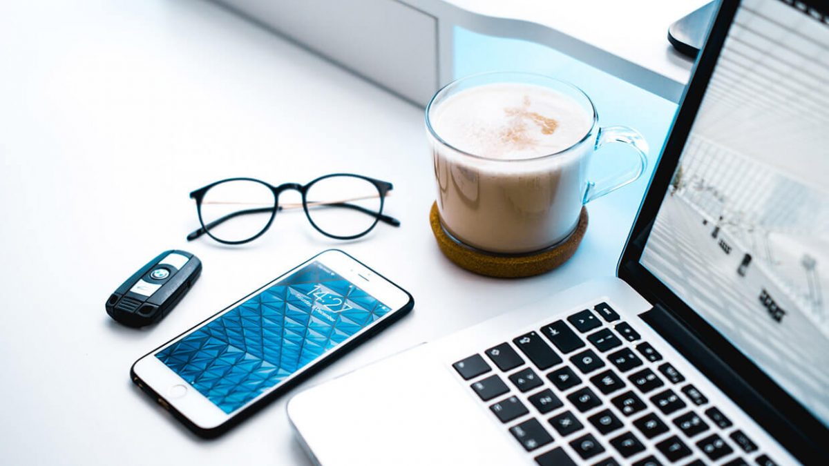 Workspace with coffee, glasses, smartphone, and laptop keyboard.