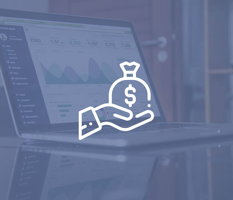 Hand holding a money bag icon in front of a laptop with financial charts.